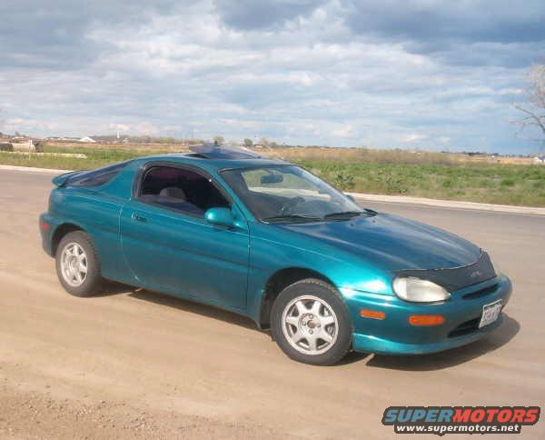 Teal 1994 Mazda MX-3 coupe parked on a dirt road with a cloudy sky