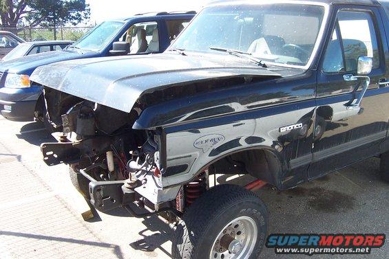 Black Ford Bronco with front end damage, missing grille and headlights. Visible "BRONCO" badge on fender
