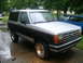1989 Ford Bronco II - A two-tone Ford Bronco II is parked on a wet driveway with trees and houses in the background.