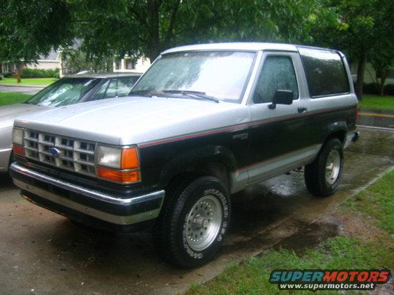 Two-tone black and silver 1989 Ford Bronco II with chrome trim and aftermarket wheels parked on a wet driveway