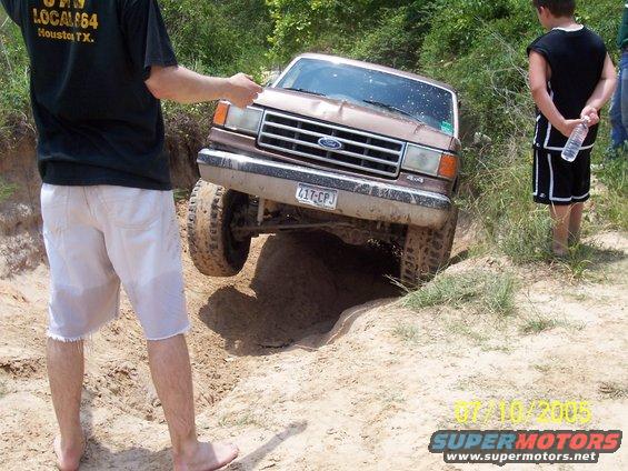 Ford Bronco with one front wheel in a ditch, people watching