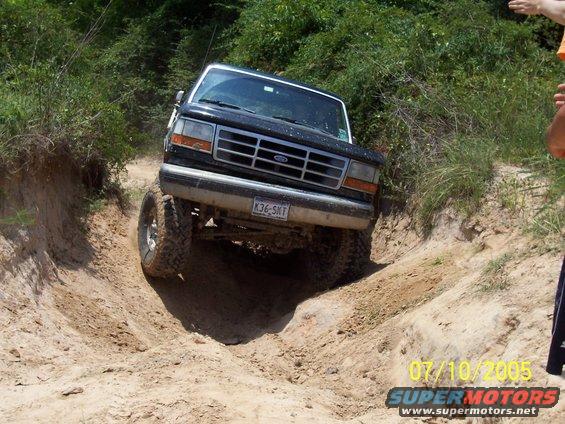 Black 1992 Ford Bronco with lifted suspension driving down a dirt path