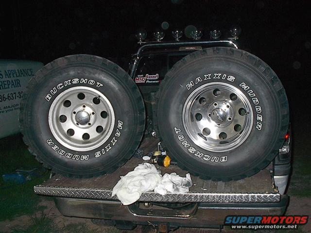 Two Maxxis Buckshot Mudder tires on chrome rims are loaded in the bed of a pickup truck