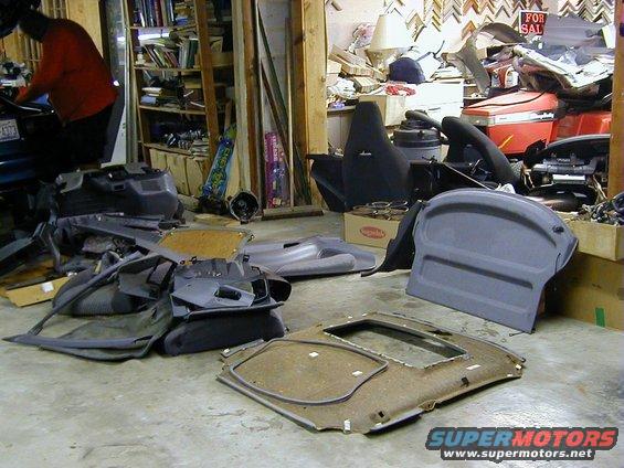 Car interior parts like seats, door panels, and headliner are spread out on a garage floor