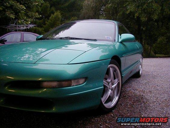 Green 1994 Ford Probe parked on gravel, trees in background. Another car is partially visible to the left
