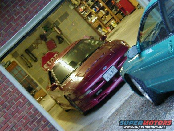 Red coupe parked next to teal sedan in a garage. Stop sign visible on the coupe's hood