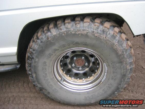 Close-up of a muddy off-road tire with 'Dunlop Radial Mud Rover' text on the sidewall. The wheel is black with a chrome lip