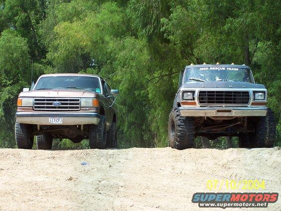 Two lifted trucks on a dirt hill, one brown Ford and one gray Ford with 'JEEP RESCUE TEAM' on top