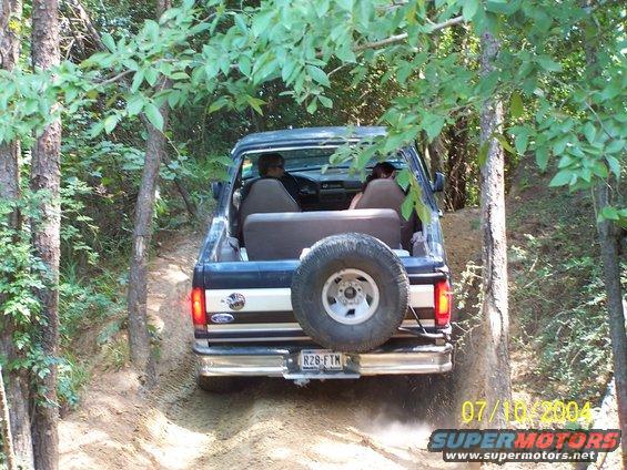1987 Ford Bronco driving on a dirt trail, spare tire mounted on rear door