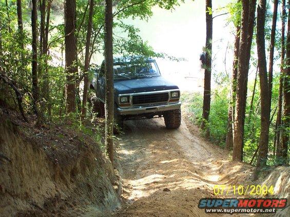 Black Ford F-Series truck on a dirt trail, front 3/4 view. Lifted suspension and off-road tires are visible