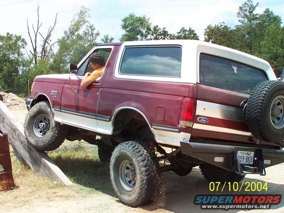 1987 Ford Bronco climbing over a wooden obstacle, rear-mounted spare tire visible