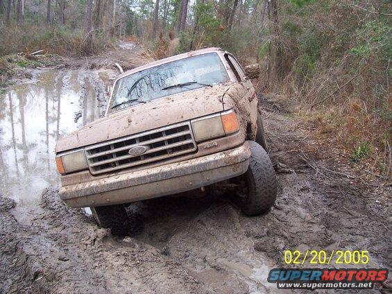Brown 1987 Ford Bronco stuck in mud on a wooded trail