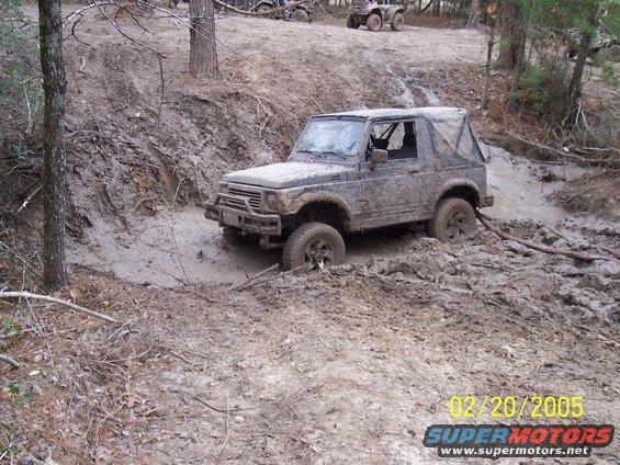Suzuki Samurai stuck in a muddy ditch, with ATVs in the background