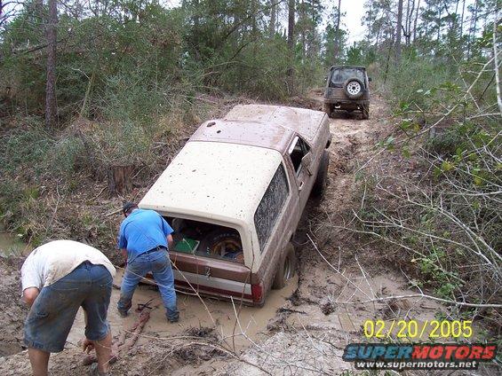 Brown 1987 Ford Bronco stuck in mud with two men nearby