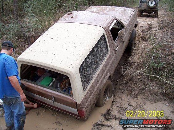 Brown and white 1987 Ford Bronco stuck in mud, with another vehicle behind