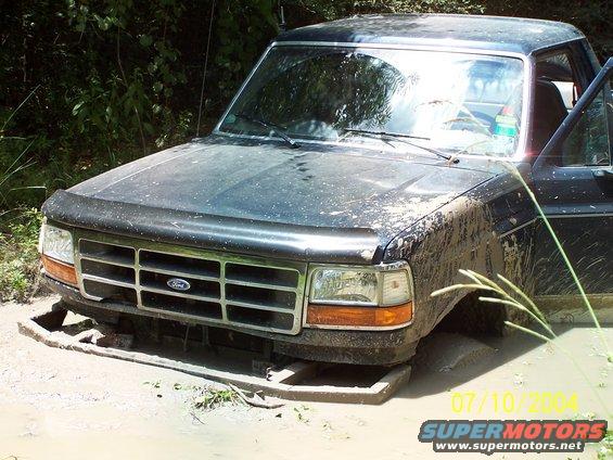 Mud-covered Ford F-series truck stuck in mud with front grille visible