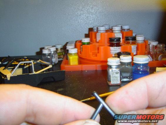 Model car chassis and paint bottles on a workbench