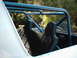 1978 Ford Bronco - The interior of a vehicle shows black quilted seats and a blue roll cage, with a spare tire in the background.