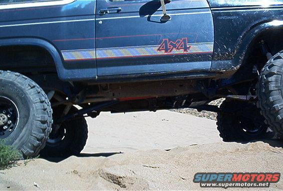 Blue Ford Bronco with 4x4 decal, lifted suspension, and large tires on sandy terrain