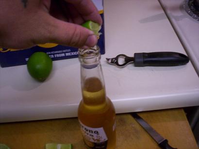Hand squeezing lime into Corona bottle, with another lime and bottle opener nearby