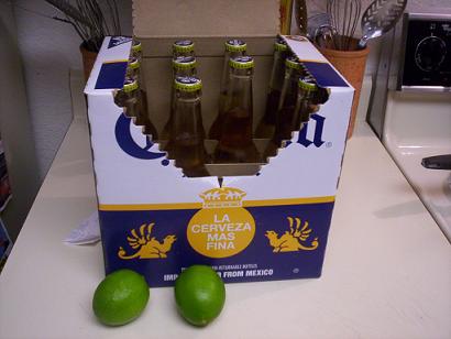 Cardboard box of Corona beer bottles with two limes on a countertop