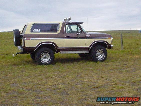 Brown and tan Ford Bronco parked in a grassy field, spare tire mounted on the rear