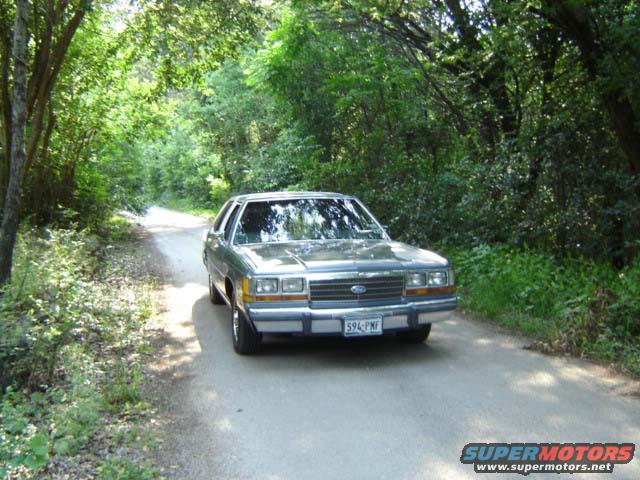 1988 Ford Crown Victoria LTD driving on a dirt road surrounded by trees