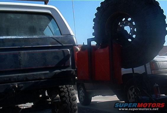 Rear of a dark Ford Bronco next to a spare tire and red jerry cans mounted on another vehicle