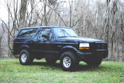 Black 1992 Ford Bronco parked on a grassy hill with trees in the background
