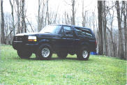Black 1992 Ford Bronco parked on grass with trees in background