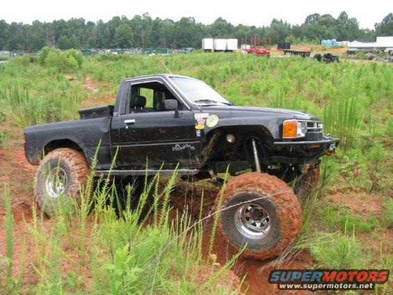 Black Toyota pickup truck with large off-road tires navigating muddy terrain