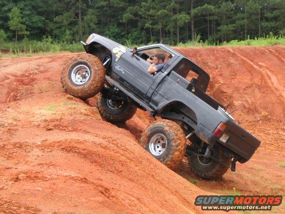 Black pickup truck with large tires climbing a steep dirt hill. Driver is visible