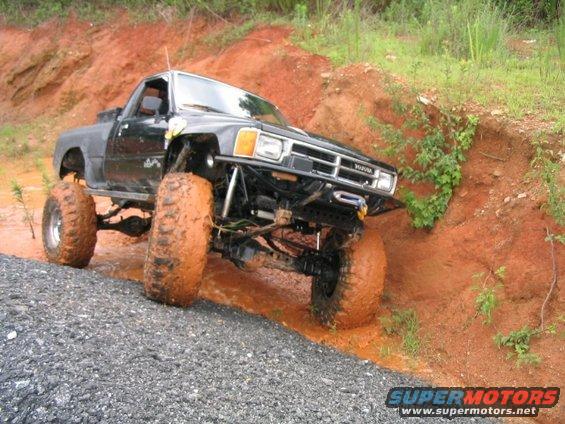 Black Toyota pickup truck with large mud tires driving through mud and gravel