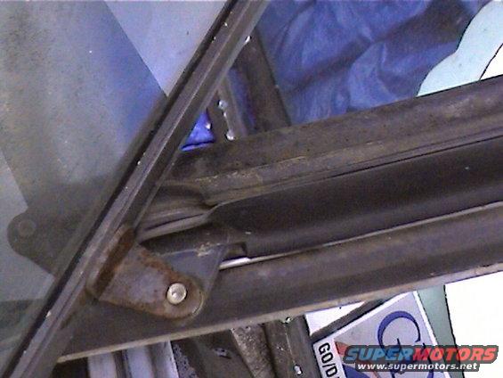 Window frame hinge with rust and blue tarp in background