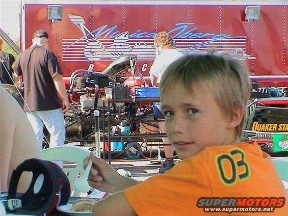 Dominik eating birthday cake with a top fuel dragster behind him