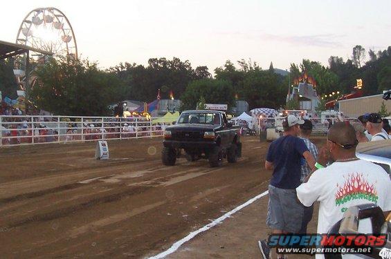 Black 1994 Ford F-150 pickup truck with lifted suspension on a dirt track at a fair