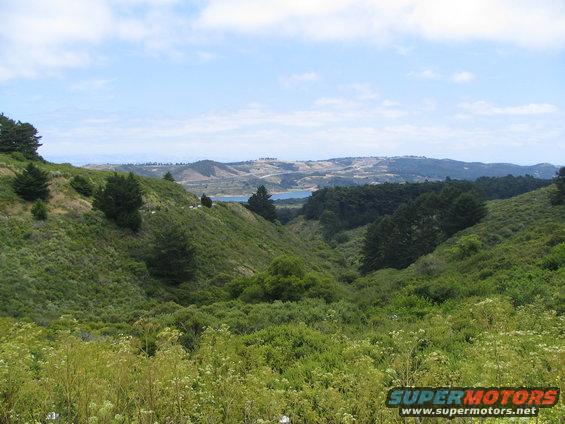 Scenic landscape with rolling green hills and a distant body of water under a partly cloudy sky