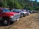 1994 Ford F-150 - Several pickup trucks are parked in a dirt lot under a tree line.
