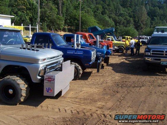Several modified pickup trucks lined up on dirt, some with large exhaust stacks. One has a 'Chase Chevrolet' sticker
