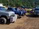 1994 Ford F-150 - A lineup of custom trucks, some with prominent exhaust pipes, parked on a dirt lot under a sunny sky.