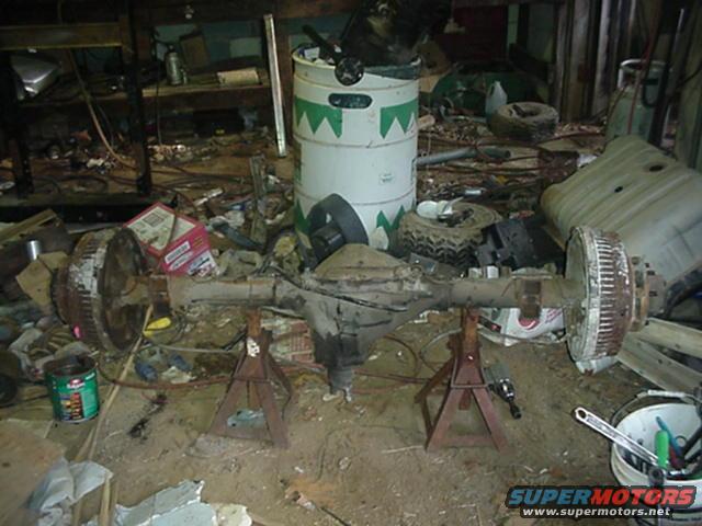 Rear axle assembly on jack stands, rusty drum brakes, in cluttered garage