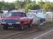 1994 Ford F-150 - A red Ford pickup truck, likely from the late 1970s, competes in a pull event, dragging a heavy sled across the dirt track.