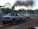 1994 Ford F-150 - Dodge Ram truck competes in a tractor pull, emitting heavy black smoke. A Ferris wheel is visible in the background.
