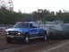1994 Ford F-150 - A blue pickup truck competes in a pull event, with a sled emitting dark smoke behind it.