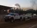 1994 Ford F-150 - A white pickup truck with flame decals tows a trailer past a Ferris wheel and grandstands at an outdoor event.