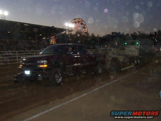Maroon pickup truck with chrome wheels pulling a trailer, Ferris wheel in background