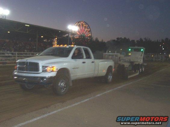 White dually pickup truck towing a trailer at dusk with a Ferris wheel in the background