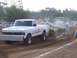 1994 Ford F-150 - A white Ford pickup truck competes in a pull event, dragging a trailer across a dirt track.