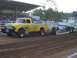1994 Ford F-150 - A vintage yellow Ford pickup truck, customized with flame graphics, competes in a pull event, dragging a weighted sled.