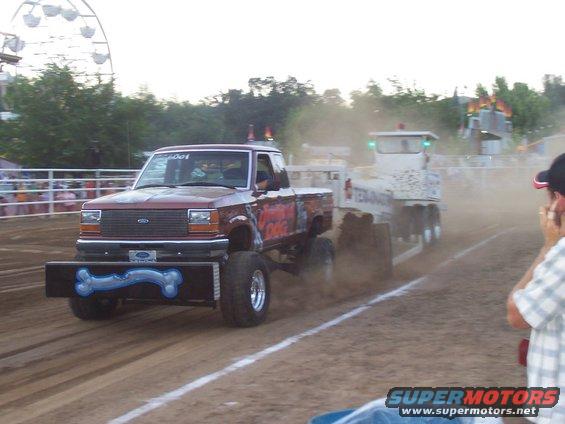Modified pickup truck with bone-themed bumper pulling a trailer in a dirt arena